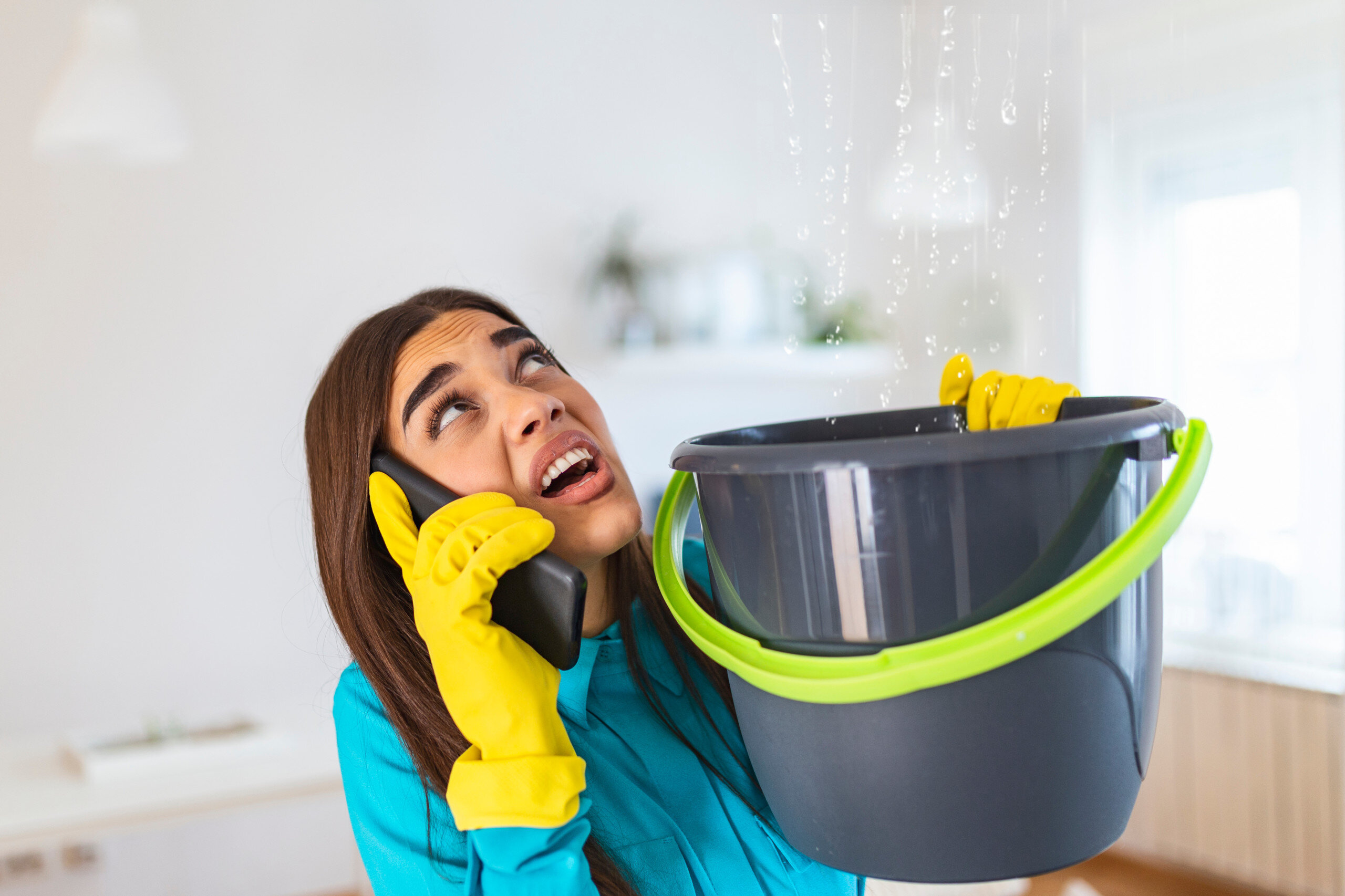 Young woman holding bucket from roof leak in her home